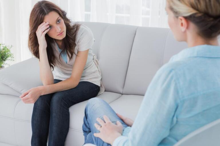 Two women discussing addiction advice on a sofa, seeking help.