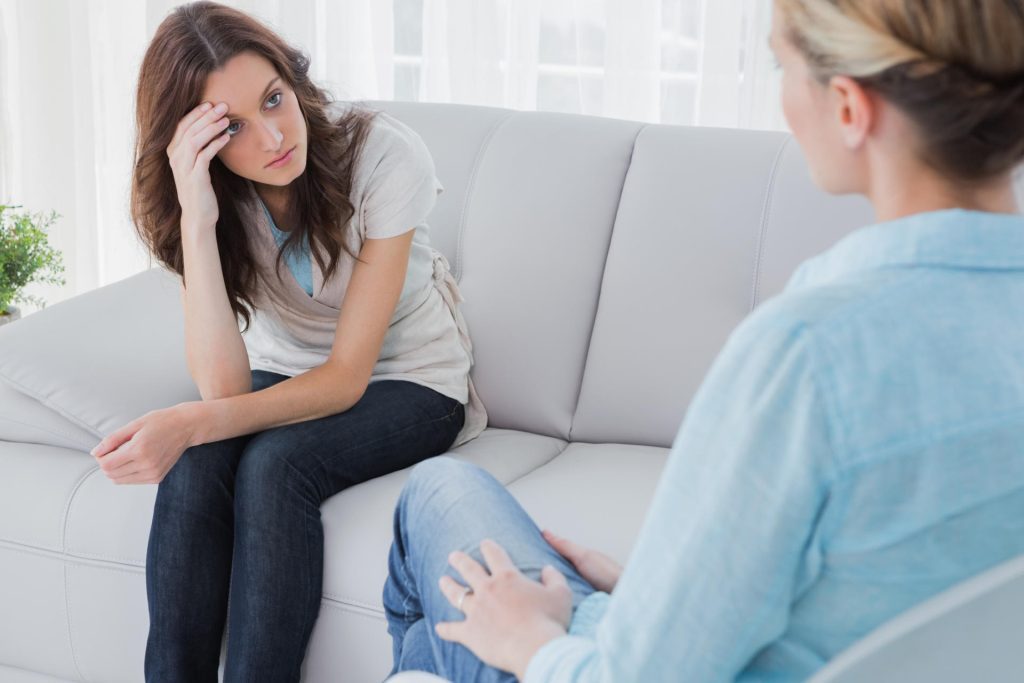 Two women discussing addiction advice on a sofa, seeking help.