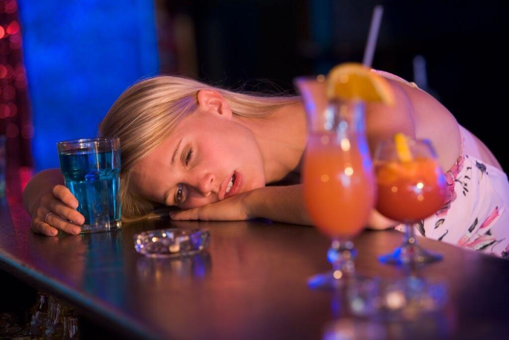 Young woman at bar, appearing intoxicated, highlighting alcohol abuse