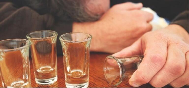 Man with empty shot glasses emphasizing alcohol addiction