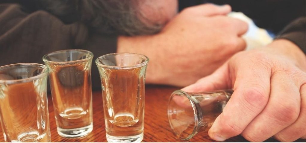 Man with empty shot glasses emphasizing alcohol addiction