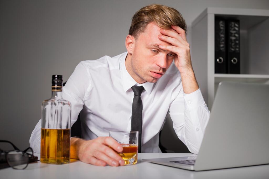 Man in distress at desk with alcohol bottle, seeking recovery