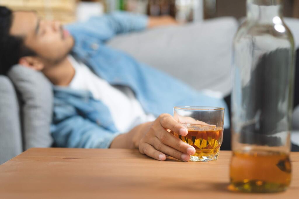 Man holding whiskey glass on couch, contemplating alcohol rehab