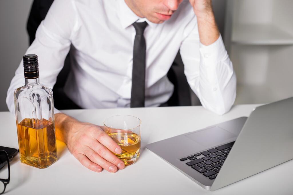 Man holding whiskey glass at desk, considering rehab options