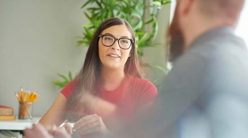 Woman in glasses talking to a man at an alcohol recovery meeting
