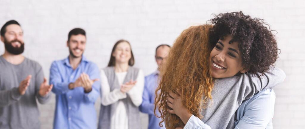 Group of people clapping as two women hug, symbolizing support in rehab