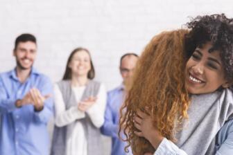 Group of people clapping as two women hug, symbolizing support in rehab