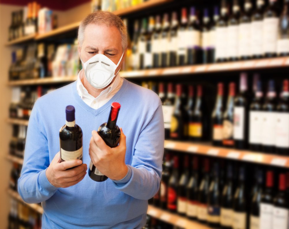 Man in mask examining wine bottles in store, considering alcohol recovery