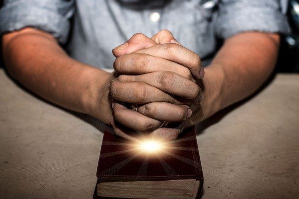 Hands praying over Bible, symbolizing faith in Christian rehab