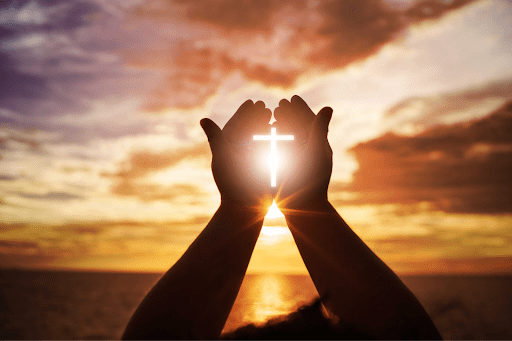 Hands holding cross at sunset, symbolizing faith in Christian rehab alcohol recovery.