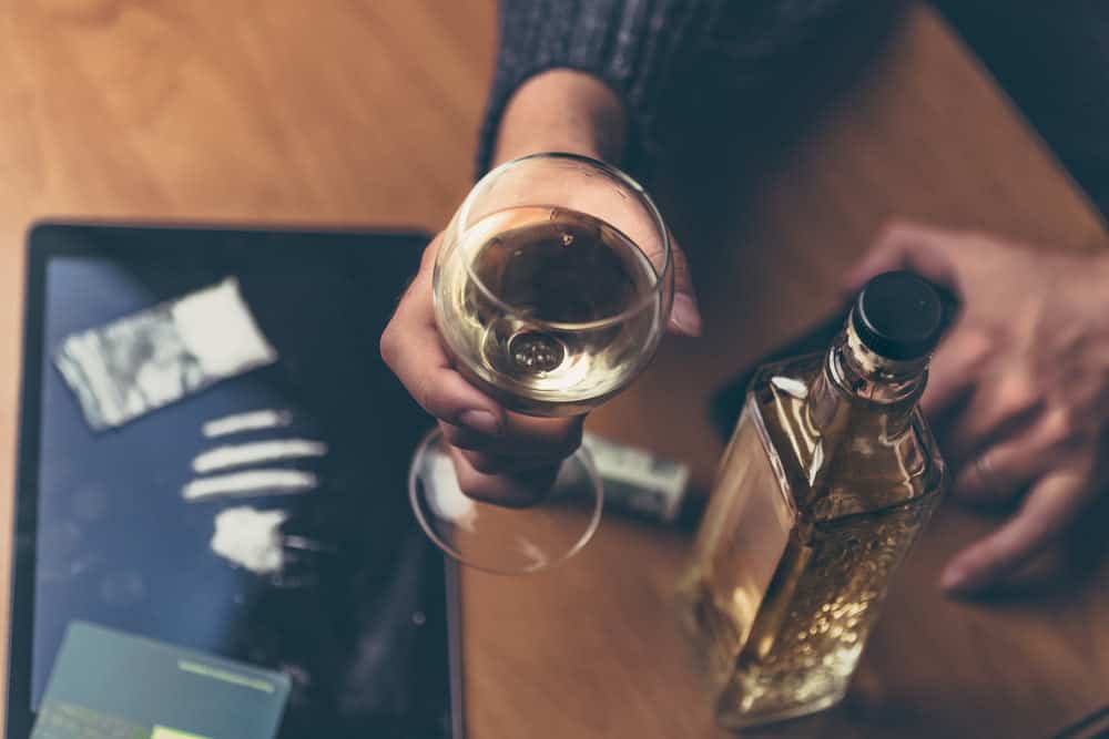 Person holding wine glass with cocaine and alcohol on table
