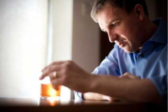 Man reflecting with glass of alcohol, thinking about quitting drinking
