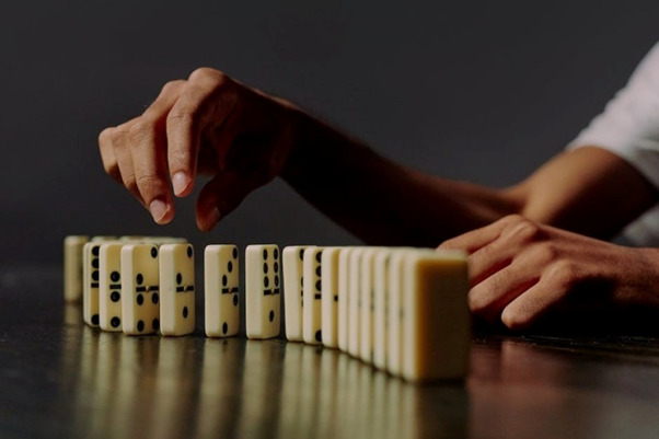 Hand arranging dominoes on table, symbolizing alcohol recovery journey.
