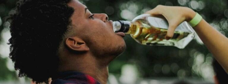 Person drinking from bottle, highlighting effects of alcohol consumption