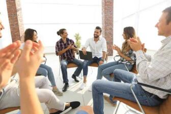 Group of people in recovery clapping during alcohol support meeting