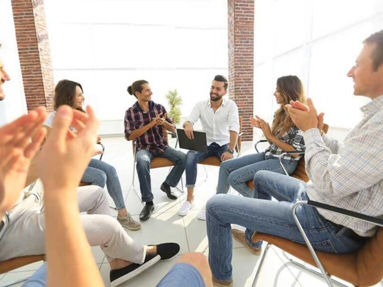 Group of people in recovery clapping during alcohol support meeting