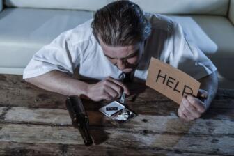 Man struggling with alcohol, holding help sign, feeling trapped; how to beat addiction