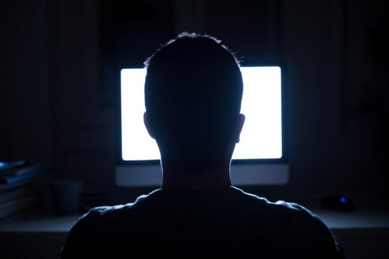 Silhouette of a person facing a computer screen, highlighting internet addiction.