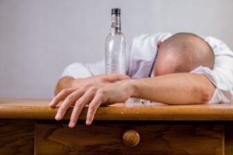 Man asleep on table with empty alcohol bottle, liver disease symptoms