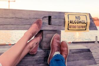 A pair of legs resting near a "No Alcohol" sign by the water.