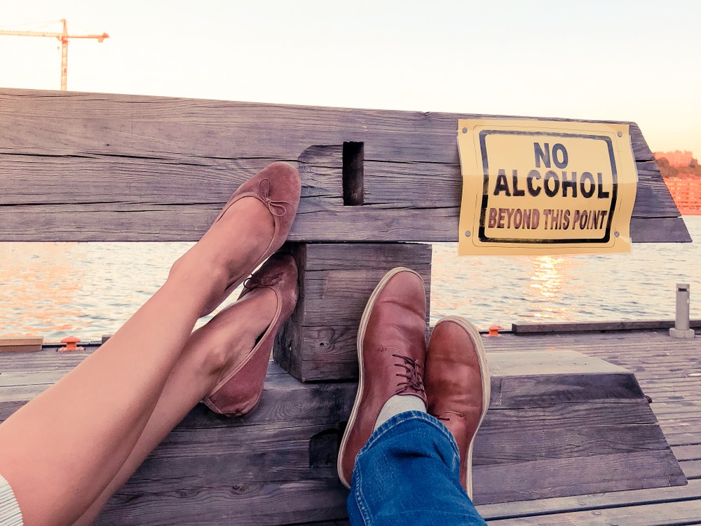 A pair of legs resting near a "No Alcohol" sign by the water.