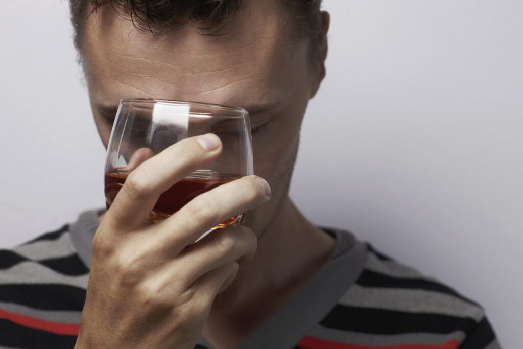 Man reflecting while holding a glass of alcohol, symbolizing addiction.