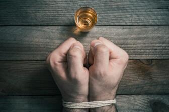 Bound hands in front of alcohol glass, symbolizing alcohol cravings battle