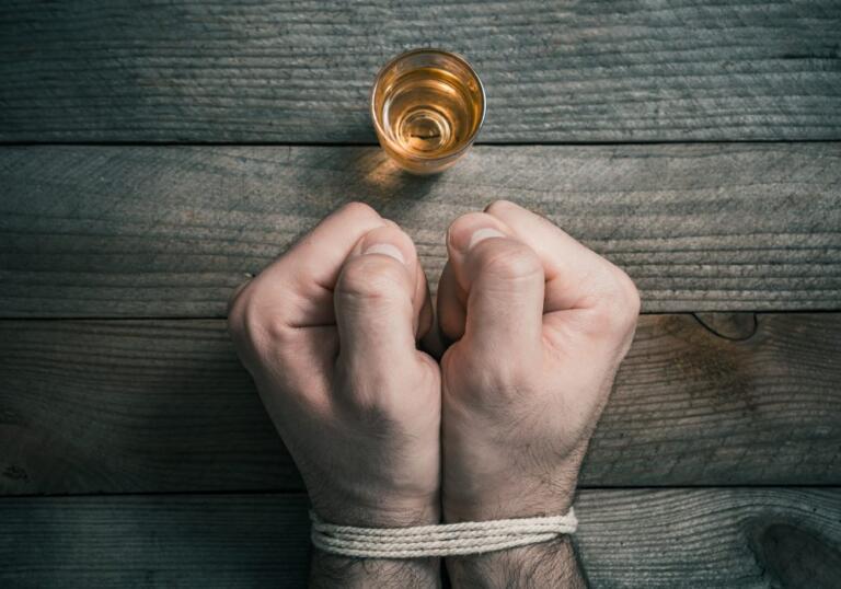 Bound hands in front of alcohol glass, symbolizing alcohol cravings battle