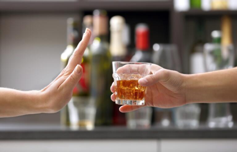 Hand refusing a glass of whiskey, symbolizing alcohol recovery