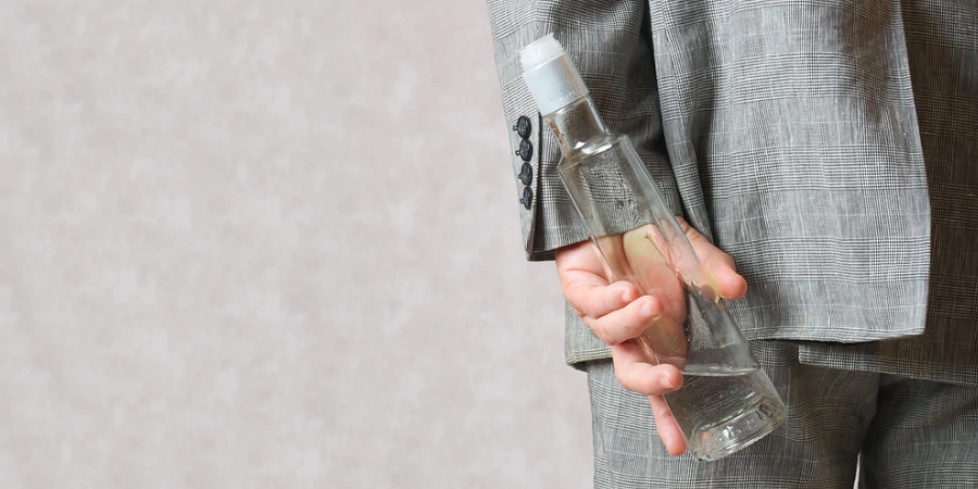 Person hiding alcohol bottle behind back, illustrating secret drinking.