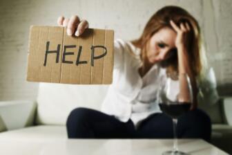 Woman holding help sign, wine glass nearby; seeking alcohol recovery