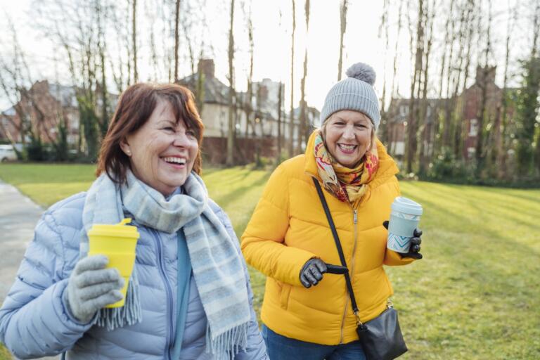 Two women walking in a park with coffee, illustrating sober companion support.