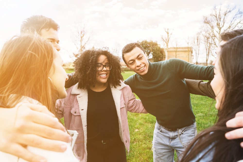 Diverse group bonding outdoors at a sober living house, smiling.