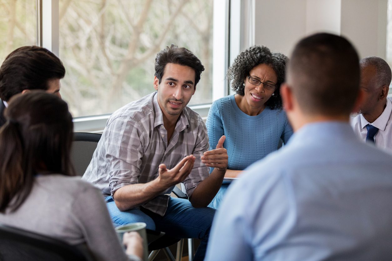 Diverse group discussing sobriety tags in support group meeting