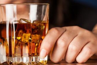 Close-up of a hand holding a glass of whiskey, symbolizing alcohol recovery