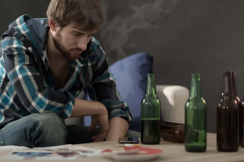 Man contemplating among empty beer bottles on table