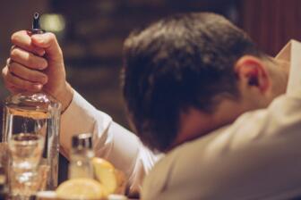 Man with head down holding an empty bottle, seeking alcohol recovery