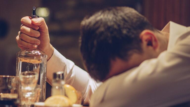 Man with head down holding an empty bottle, seeking alcohol recovery
