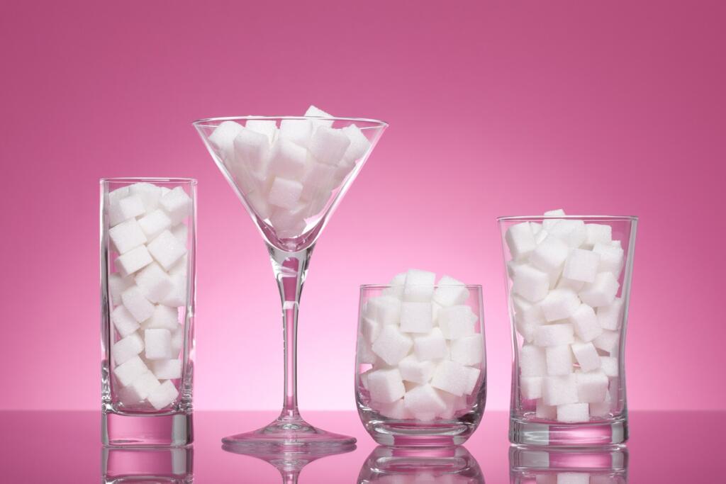 Four glasses filled with sugar cubes against pink background