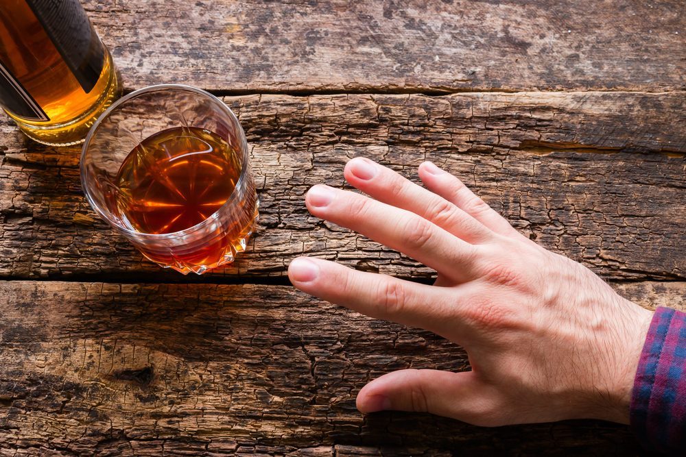 Hand reaching for a glass of alcohol, showing symptoms of alcohol poisoning risk