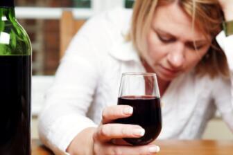 Woman struggling with alcoholism, holding wine, seeking help