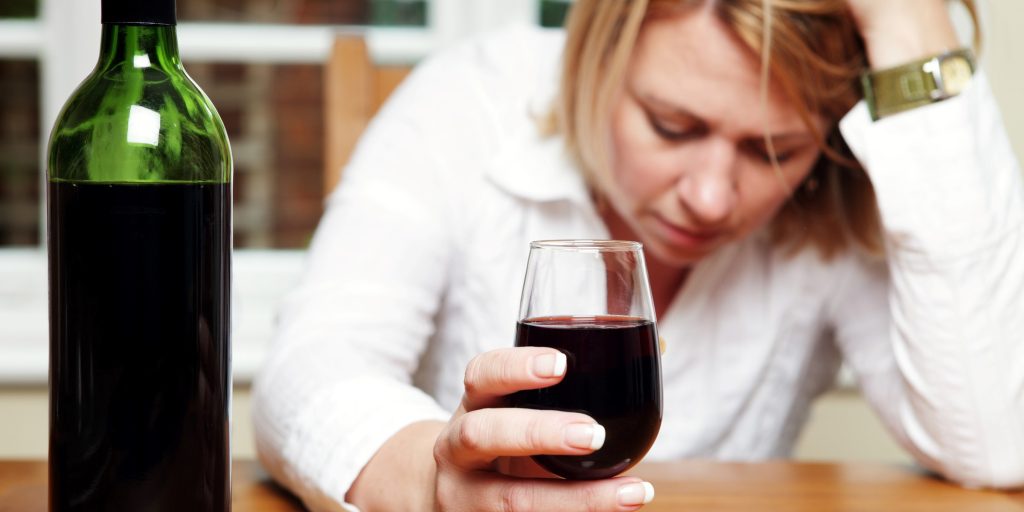 Woman struggling with alcoholism, holding wine, seeking help