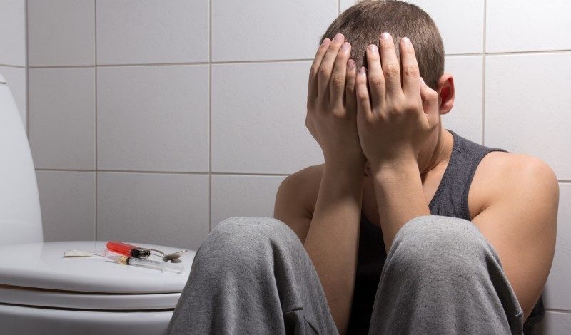 Man struggling with heroin addiction sitting on bathroom floor